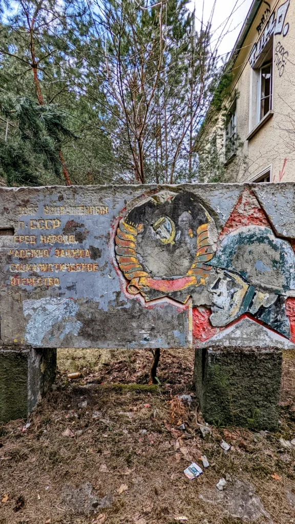 Betonrelief mit kyrillischer Schrift, Wappen und Soldatenköpfen vor einem Gebäude