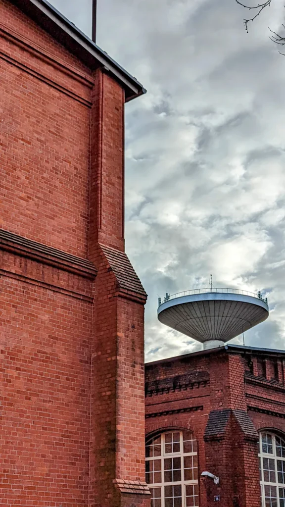 Neuer Wasserturm mit pilzförmigem Behälter hinter einer Backsteinhalle im Gaswerk Mariendorf