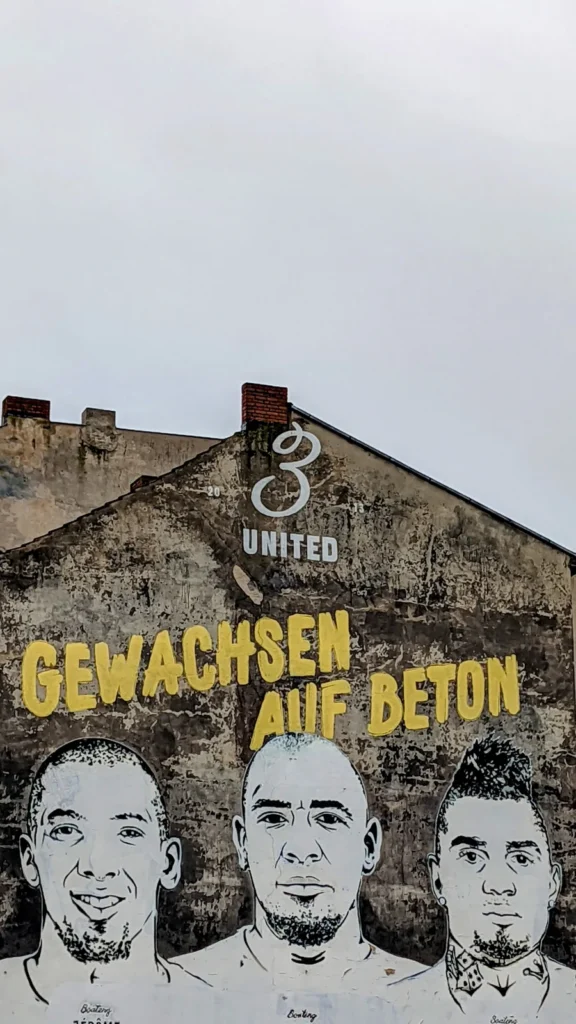 Wandbild mit den Gesichtern der drei Boateng-Brüder und gelbem Schriftzug an einer Brandwand an der Badstraße