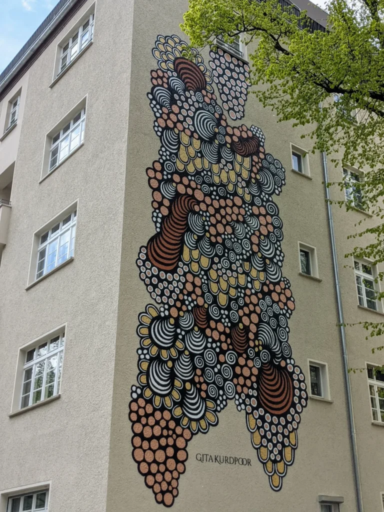 Wandbild Blossom von Gita Kurdpoor an der Leopoldstraße in Berlin-Rummelsburg: verschlungenes Muster aus Kreisen und Spiralen in Schwarz, Kupfer, Gold und Weiß an einer Hausecke
