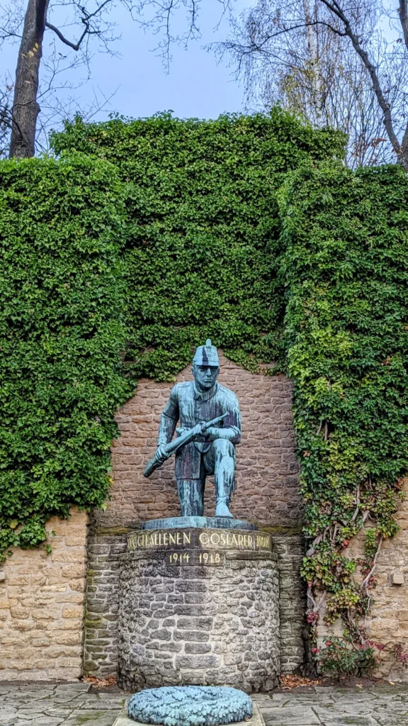 Bronzefigur eines knienden Soldaten mit Gewehr vor einer Efeumauer, auf dem Sockel „Den gefallenen Goslarer Jägern“