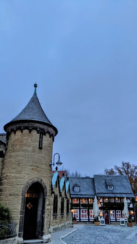 Runder Steinturm mit spitzem Dach, dahinter Fachwerkhäuser an einem Platz