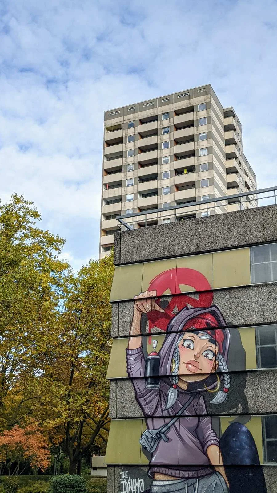 Großes Wandbild einer jungen Frau mit Spraydose am Sockel eines Hochhauses in der Gropiusstadt