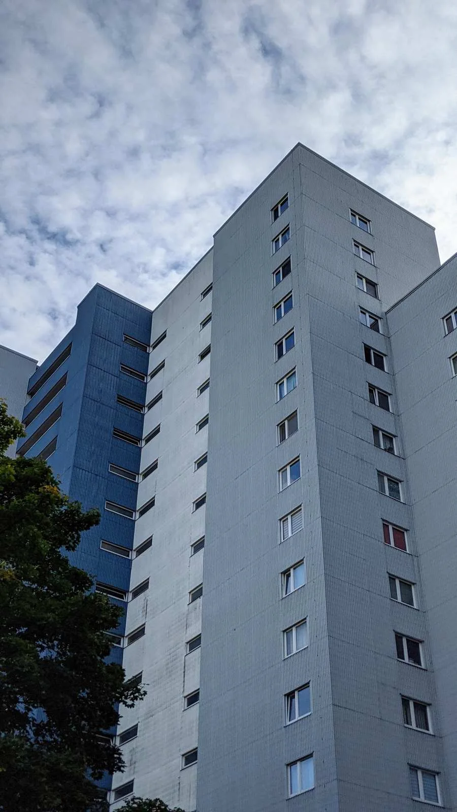 Graues Wohnhochhaus mit schmalen Fensterreihen zwischen Bäumen in der Gropiusstadt