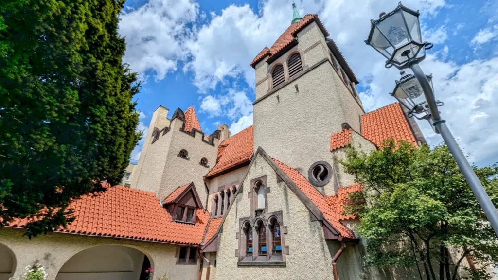 Kirche des Guten Hirten in Guben: heller Putzbau mit roten Ziegeldächern und kantigem Turm, davor eine alte Straßenlaterne