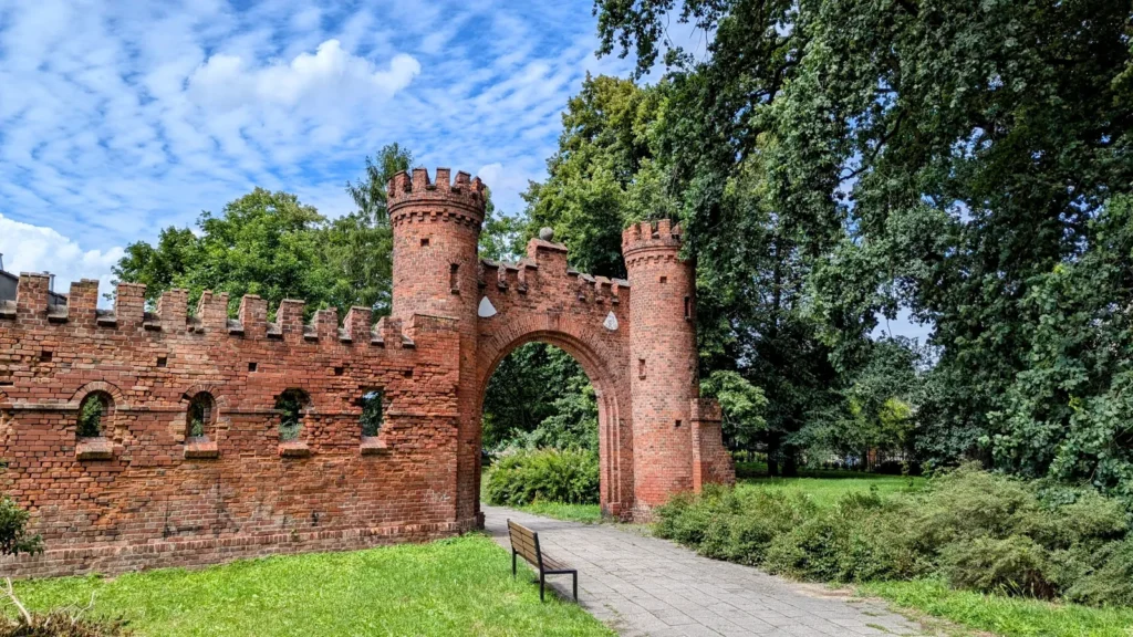 Neogotisches Backsteintor in Gubin mit zwei Türmchen und Zinnenmauer, dahinter ein Parkweg