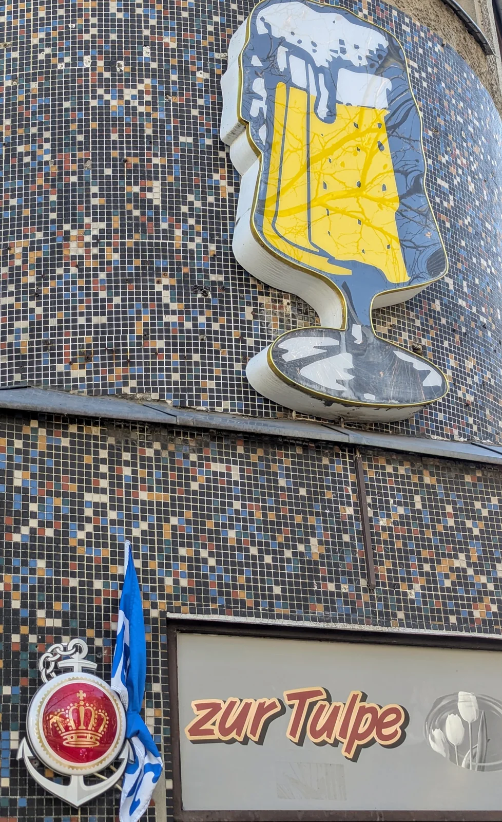 Hausreklame mit Bierglas, Krone und dem Schriftzug zur Tulpe an einer Mosaikfassade