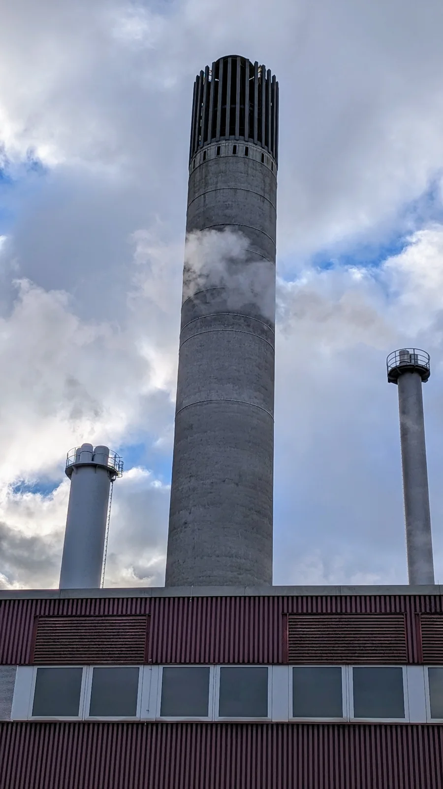 Hoher Industrieschornstein neben einem Betriebsgebäude mit weiteren Schloten