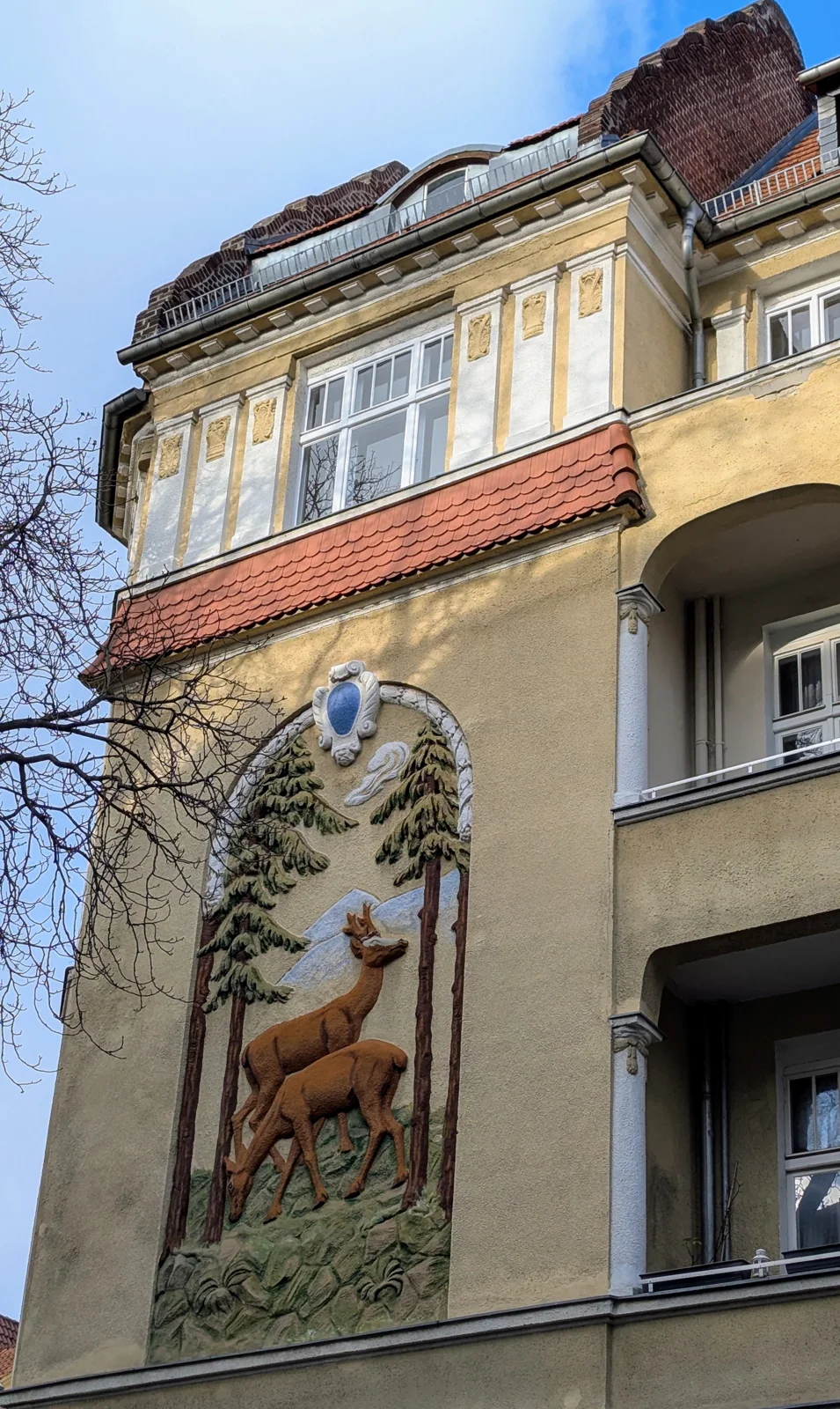 Farbiges Wandrelief mit zwei Rehen zwischen Kiefern an einer Altbaufassade