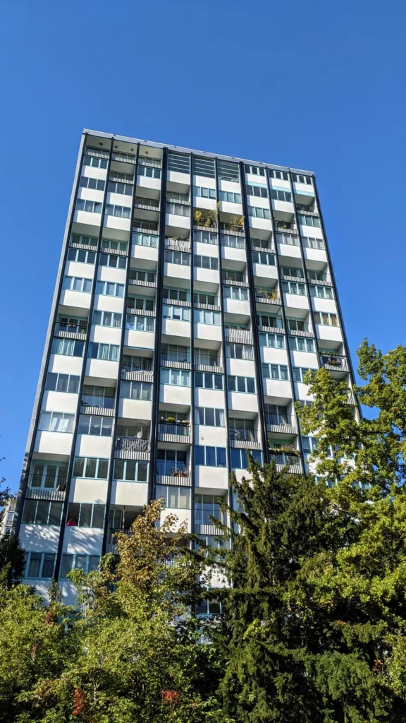 Schlankes Punkthochhaus der Interbau an der Bartningallee mit gerasterter Fassade und Balkonen über Bäumen