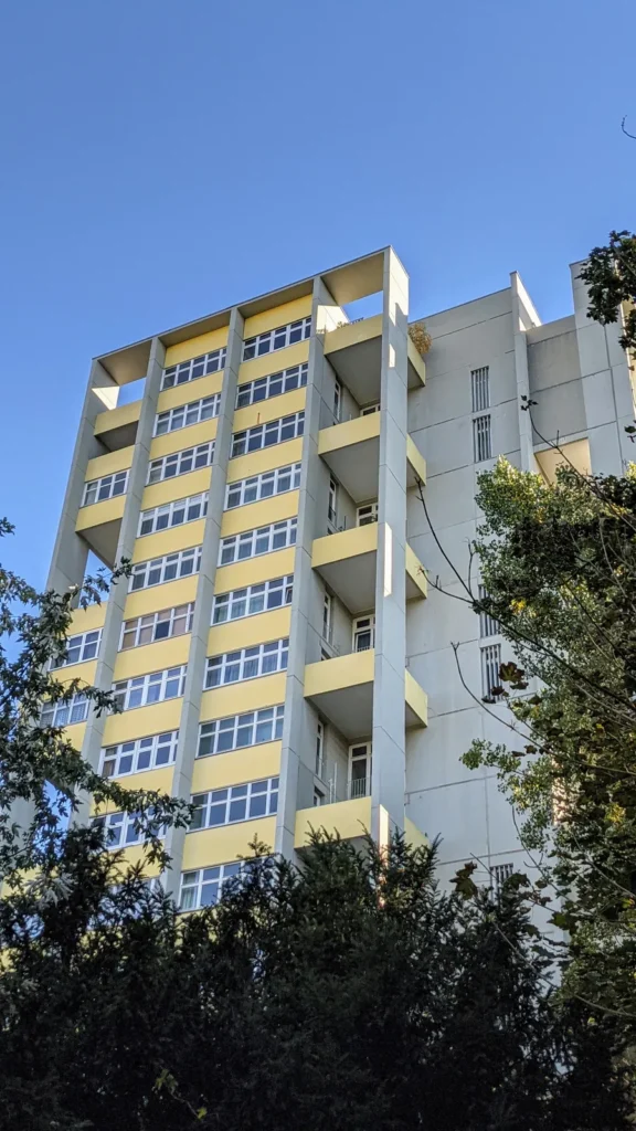 Wohnhochhaus der Interbau an der Bartningallee mit gelben Brüstungen und Betonrahmen hinter dunklen Bäumen