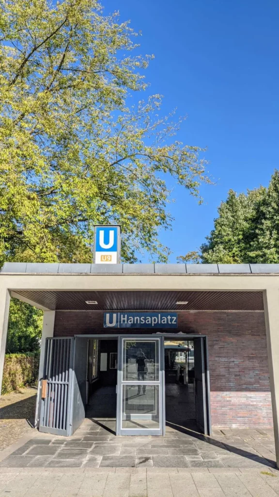 Flacher Eingangspavillon des U-Bahnhofs Hansaplatz mit U-Bahn-Schild unter herbstlichen Bäumen im Hansaviertel