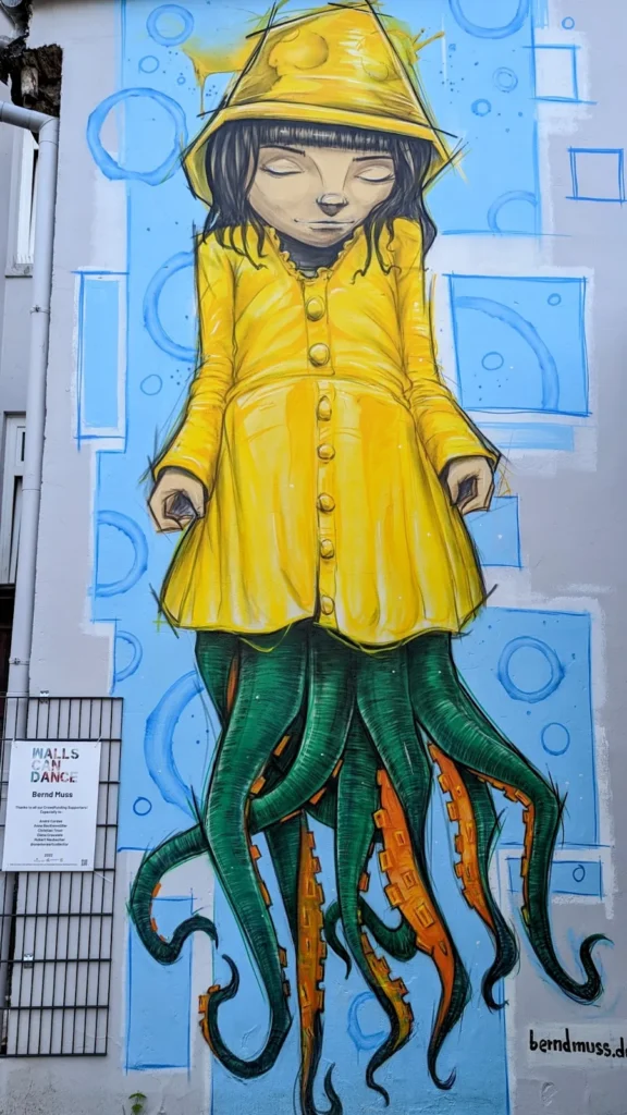 Wandbild Das Krakenmädchen aus dem Norden von Bernd Muss Am Wall 13 in Hamburg-Harburg: Mädchen in gelbem Regenmantel mit Tentakeln