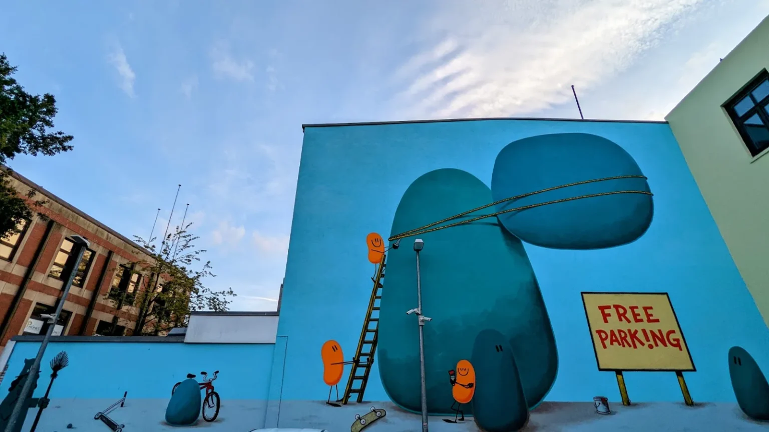 Wandbild Free Parking von Dave the Chimp Am Wall 13 in Hamburg-Harburg: orange Figuren auf blauer Wand, dazu ein Schild Free Parking