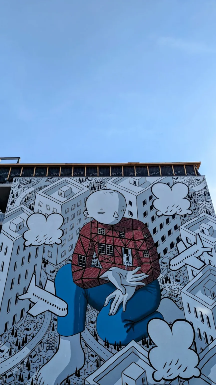 Wandbild Welcome von Millo am Wallgraben 48 in Hamburg-Harburg: kniende Figur in Schwarz-Weiß mit rotem Hemd und blauer Hose