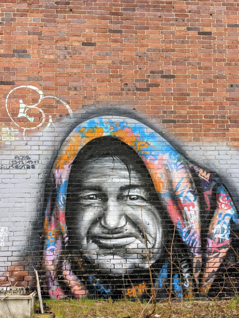 Porträt eines älteren Mannes mit bunter Kapuze auf einer Backsteinwand im Heeresbekleidungshauptamt Bernau