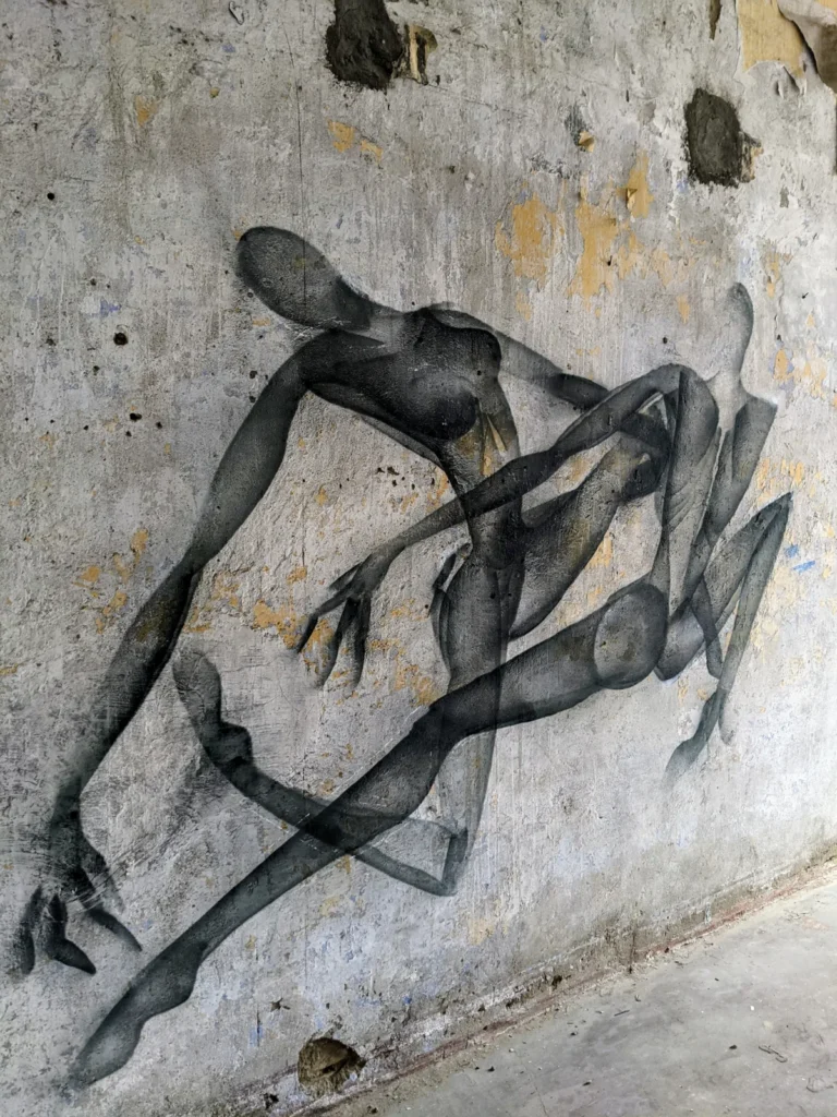 Schwarz-graue, übereinander gelegte Figuren an einer verwitterten Wand im Heeresbekleidungshauptamt Bernau
