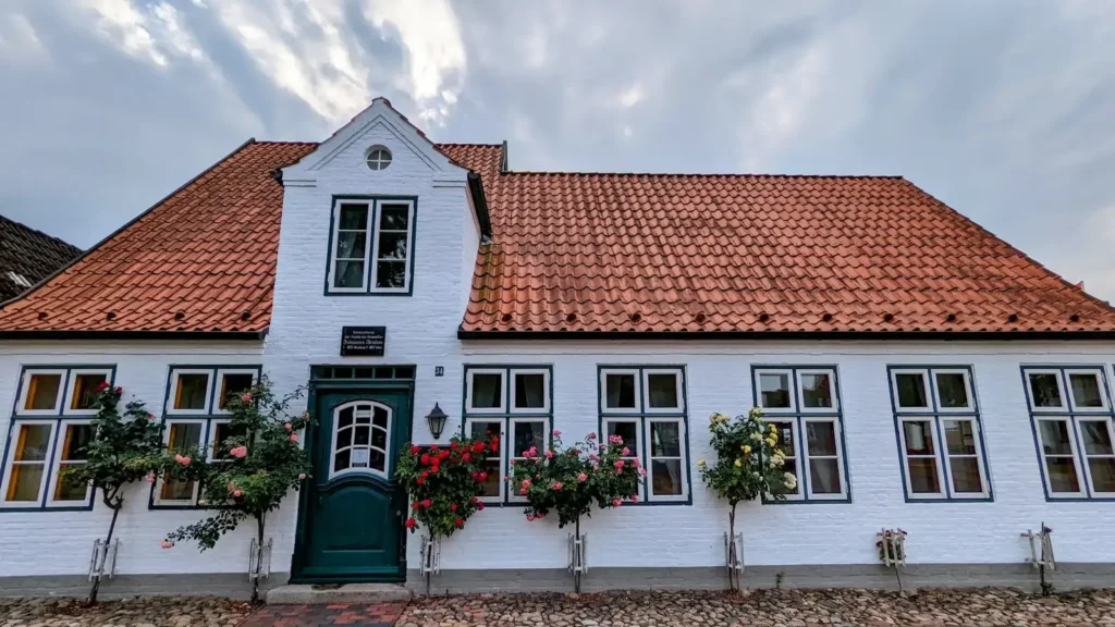 Brahms-Haus in Heide: weißes Haus mit rotem Dach, grüner Haustür und Rosen vor den Fenstern