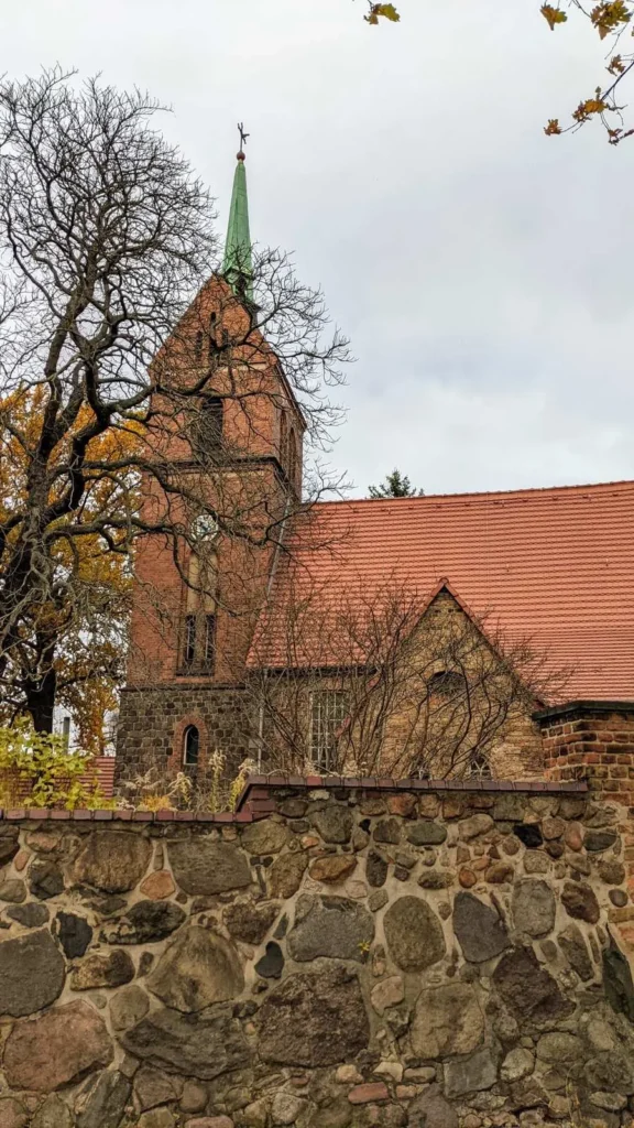 Backsteinkirche mit spitzem Turm hinter einer Feldsteinmauer, Dorfkirche in Heinersdorf