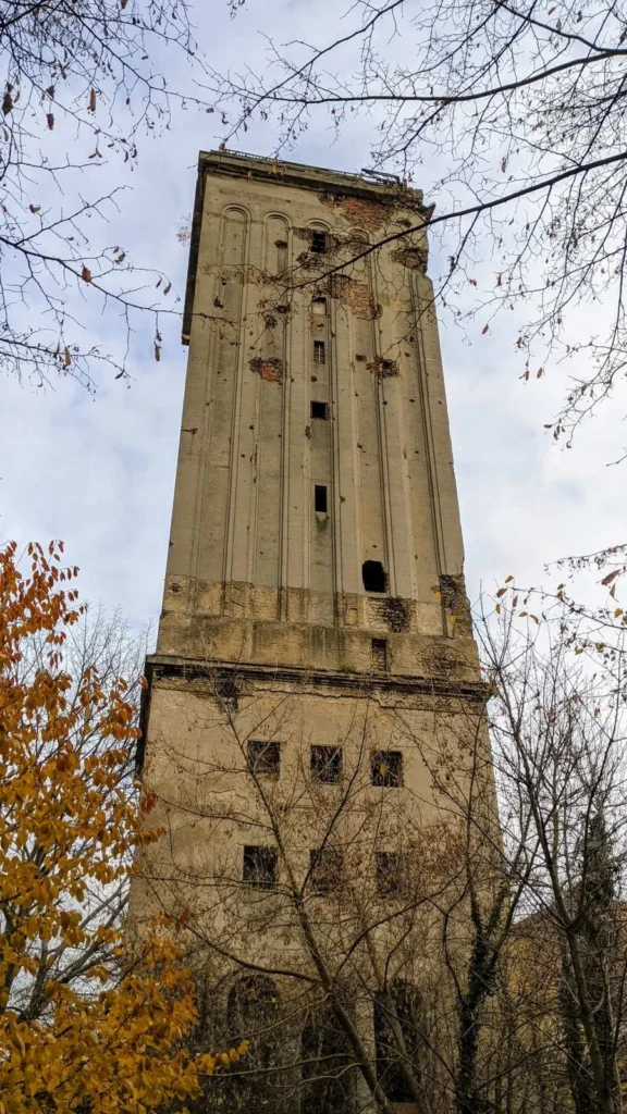 Hoher, verwitterter Wasserturm mit Pilastern und Fensteröffnungen zwischen Herbstbäumen in Heinersdorf