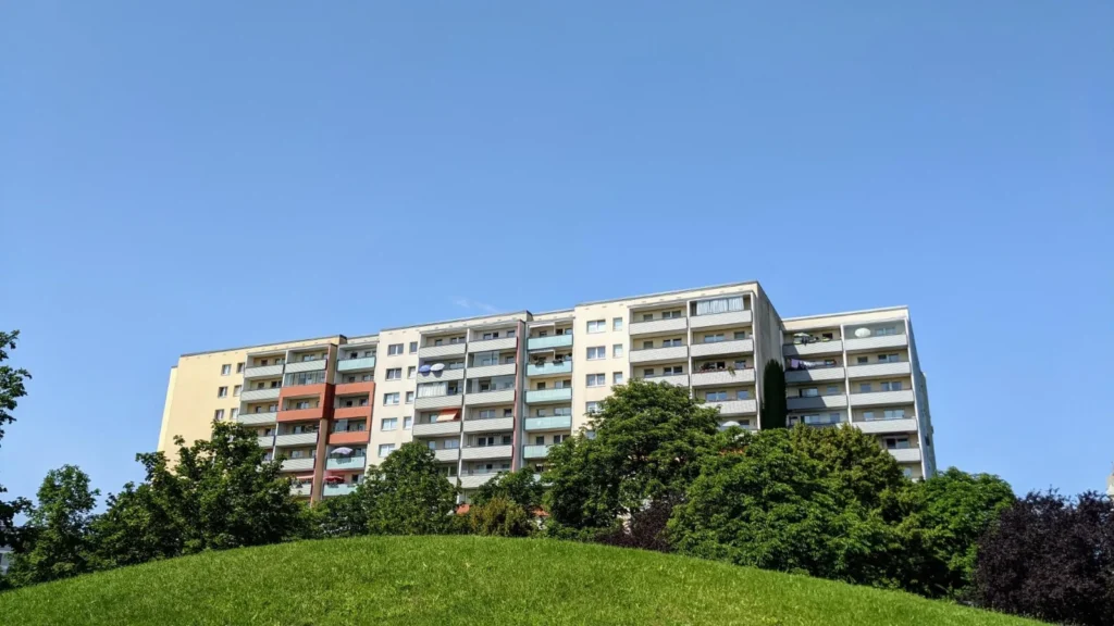 Plattenbau-Wohnblock in Hellersdorf hinter einem grünen Hügel