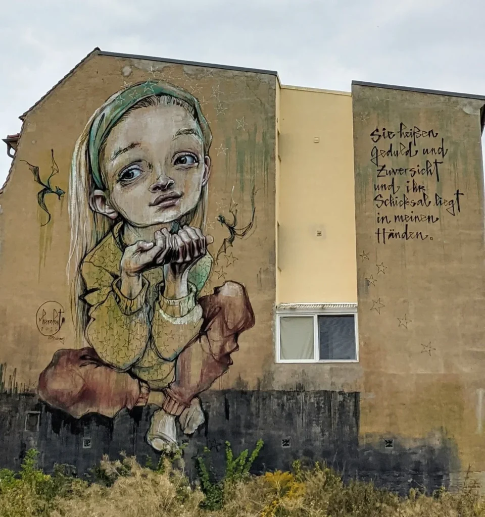 Wandbild von Herakut an der Mittelstraße in Lutherstadt Wittenberg: Mädchen mit grünem Kopftuch, zwei kleine Drachen und ein Schriftzug
