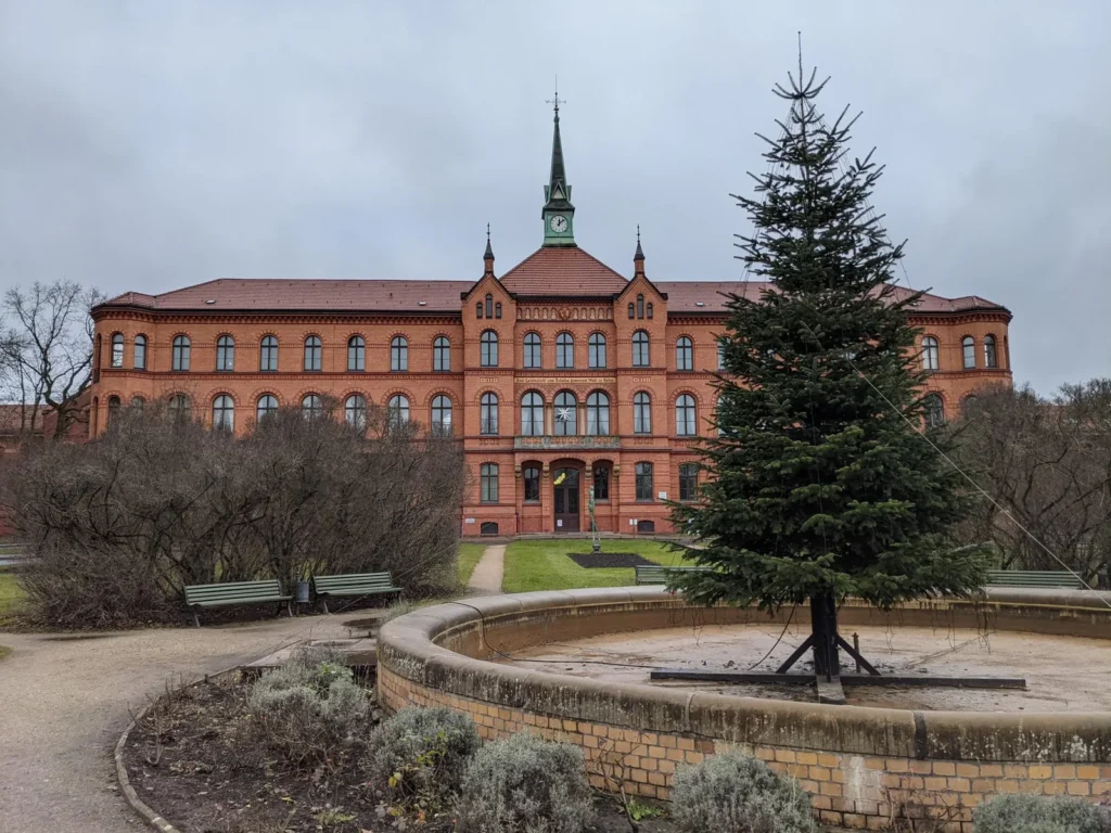 Hauptgebäude des Krankenhauses Königin Elisabeth Herzberge mit Uhrturm, davor ein Rondell mit Weihnachtsbaum