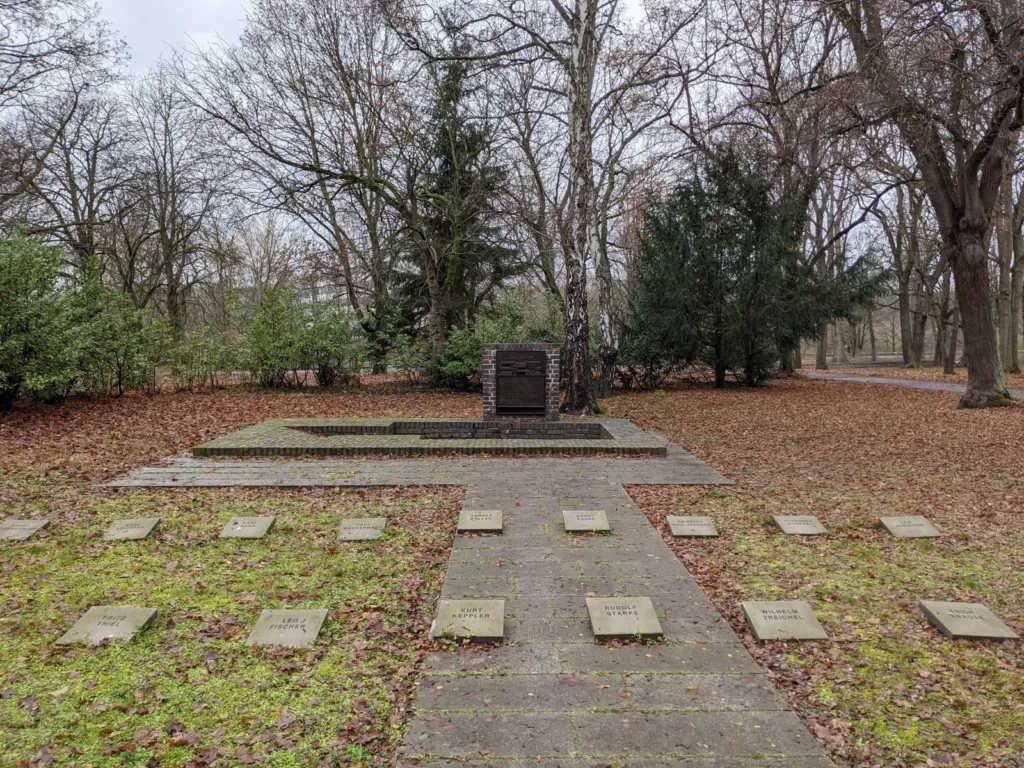 Erinnerungsmal von 1983 am Standort des Revolutionsdenkmals von Mies van der Rohe auf dem Zentralfriedhof Friedrichsfelde, ein Klinkerblock mit Bronzerelief und Grabplatten im Laub