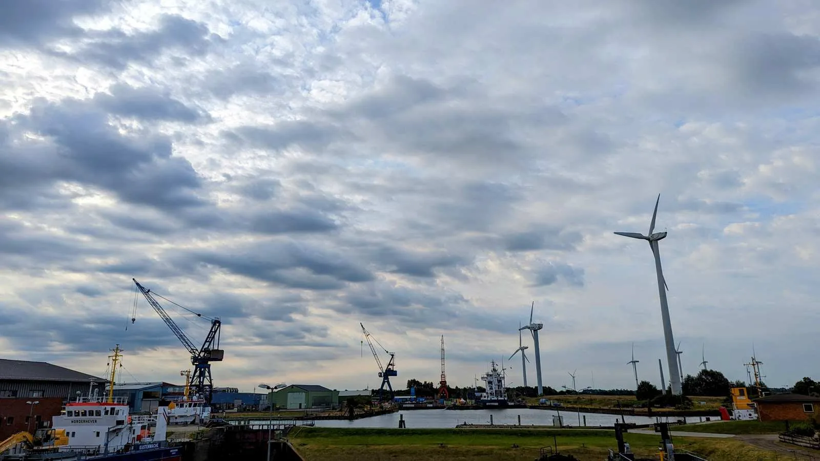 Hafen in Husum mit Kränen, Schiffen und Windrädern im Hintergrund