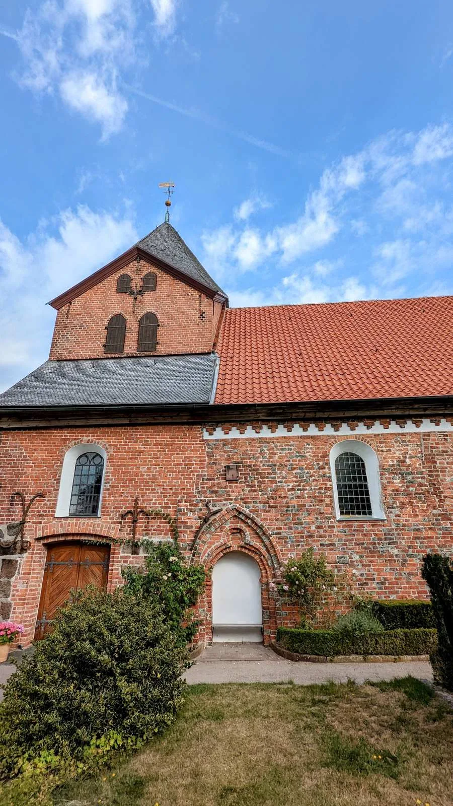 Backsteinkirche in Schobüll bei Husum mit schiefergedecktem Turmaufbau und Rosen an der Wand