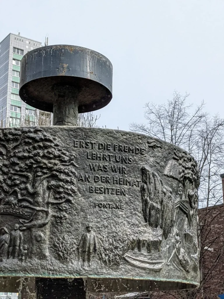 Fontanebrunnen an der Dathepromenade in Berlin-Friedrichsfelde mit Fontane-Zitat, im Hintergrund ein Hochhaus