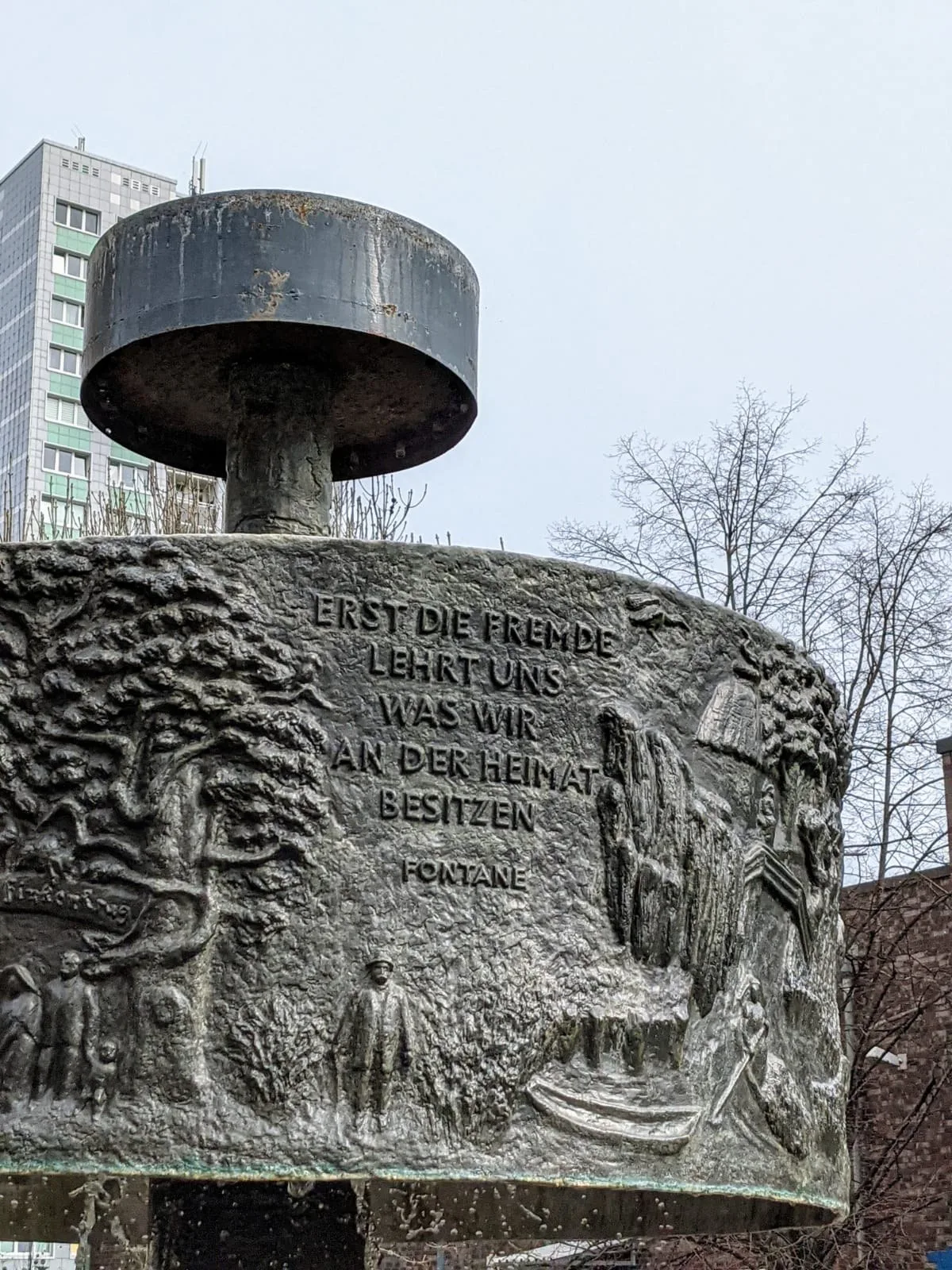 Fontanebrunnen an der Dathepromenade in Berlin-Friedrichsfelde mit Fontane-Zitat, im Hintergrund ein Hochhaus