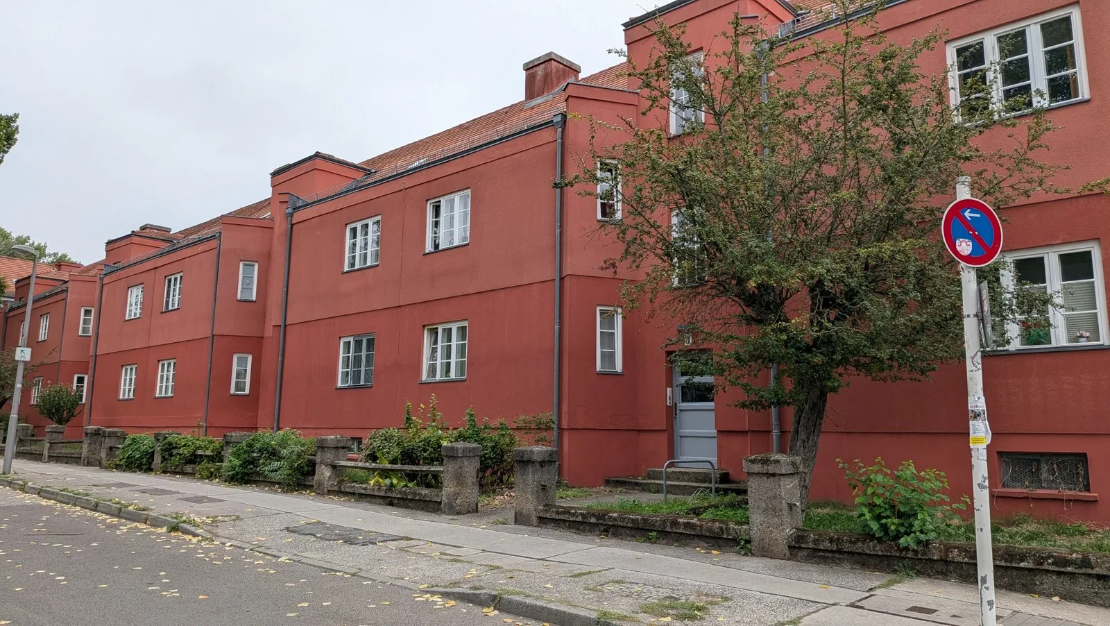 Rote Häuserzeile der Splanemann-Siedlung in Berlin-Friedrichsfelde mit Baum und Verkehrsschild