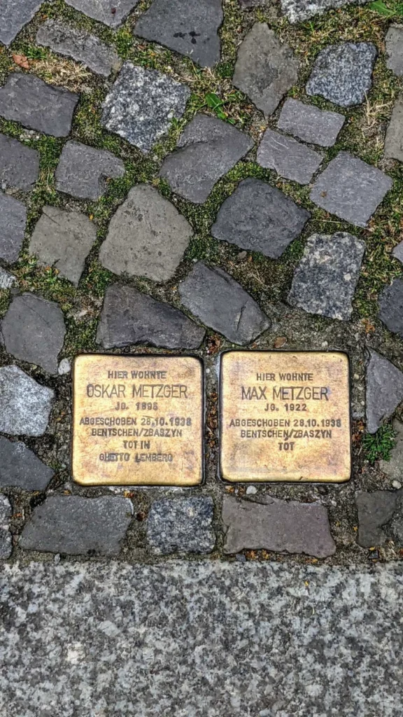 Zwei Stolpersteine für Oskar und Max Metzger nebeneinander in dunklem Kleinpflaster, unten ein Granitbord