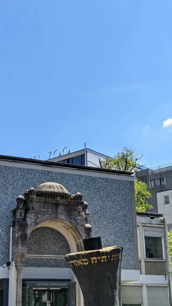 Altes Steinportal der Synagoge Fasanenstraße vor dem Jüdischen Gemeindehaus, im Vordergrund angeschnitten die Skulptur Thora-Rolle mit hebräischer Inschrift