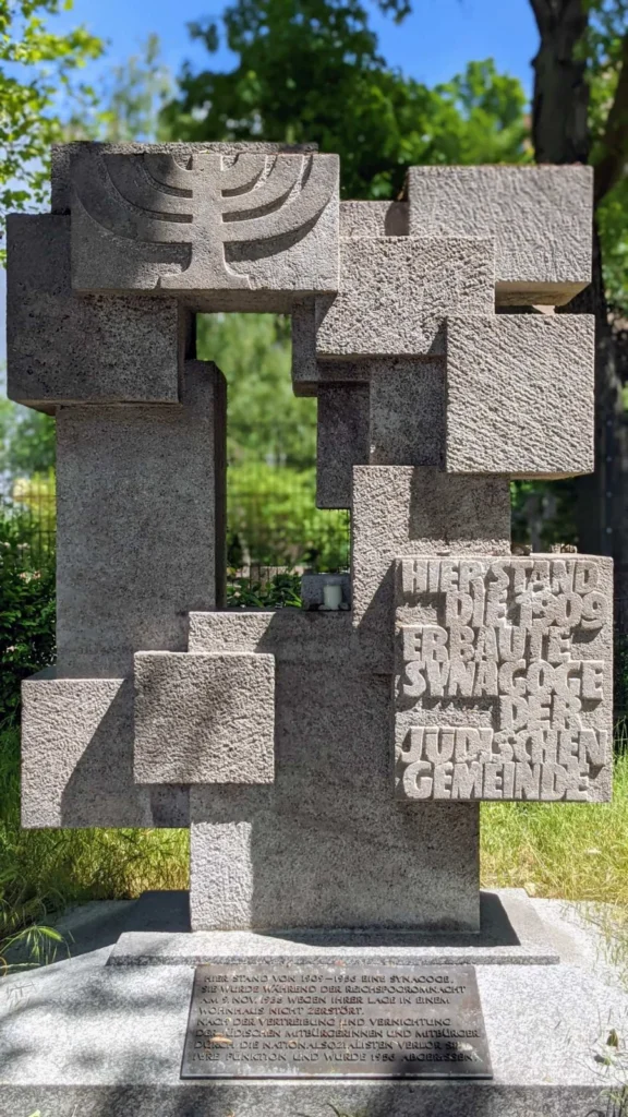 Denkmal aus versetzt gestapelten Natursteinquadern für die zerstörte Synagoge in der Münchener Straße, oben ein Relief mit siebenarmigem Leuchter