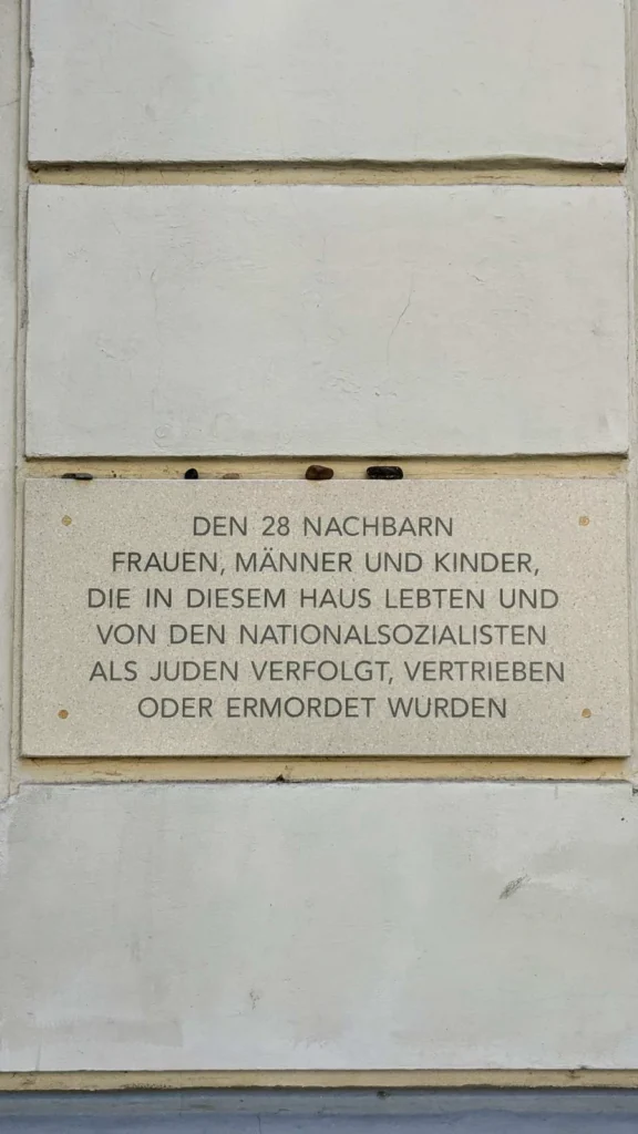 Steintafel Den 28 Nachbarn an der Hauswand der Apostel-Paulus-Straße 26 in Schöneberg, auf der Oberkante liegen Steine