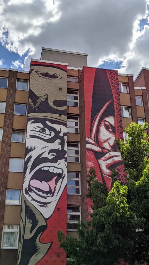Wohnhochhaus aus rotem Klinker mit dem Wandbild Israel/Palestine von Shepard Fairey, links ein schreiender Mann, rechts eine verhüllte Figur in Rot