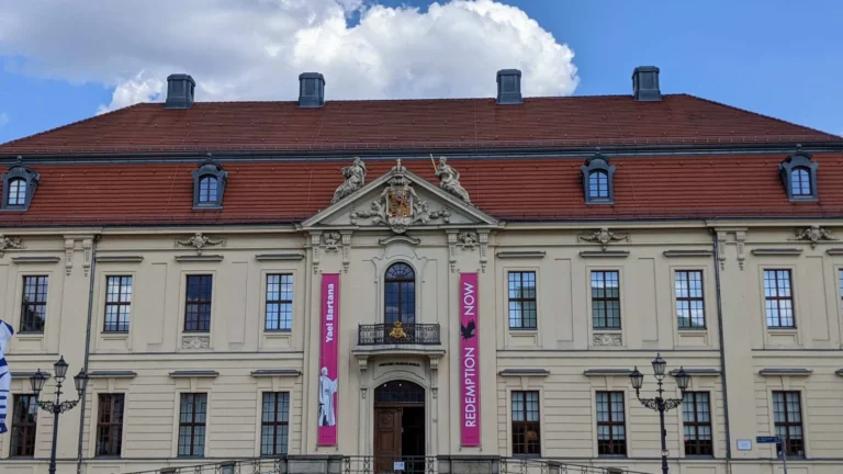 Barocker Altbau des Jüdischen Museums Berlin mit Giebel, Portal und zwei pinken Bannern