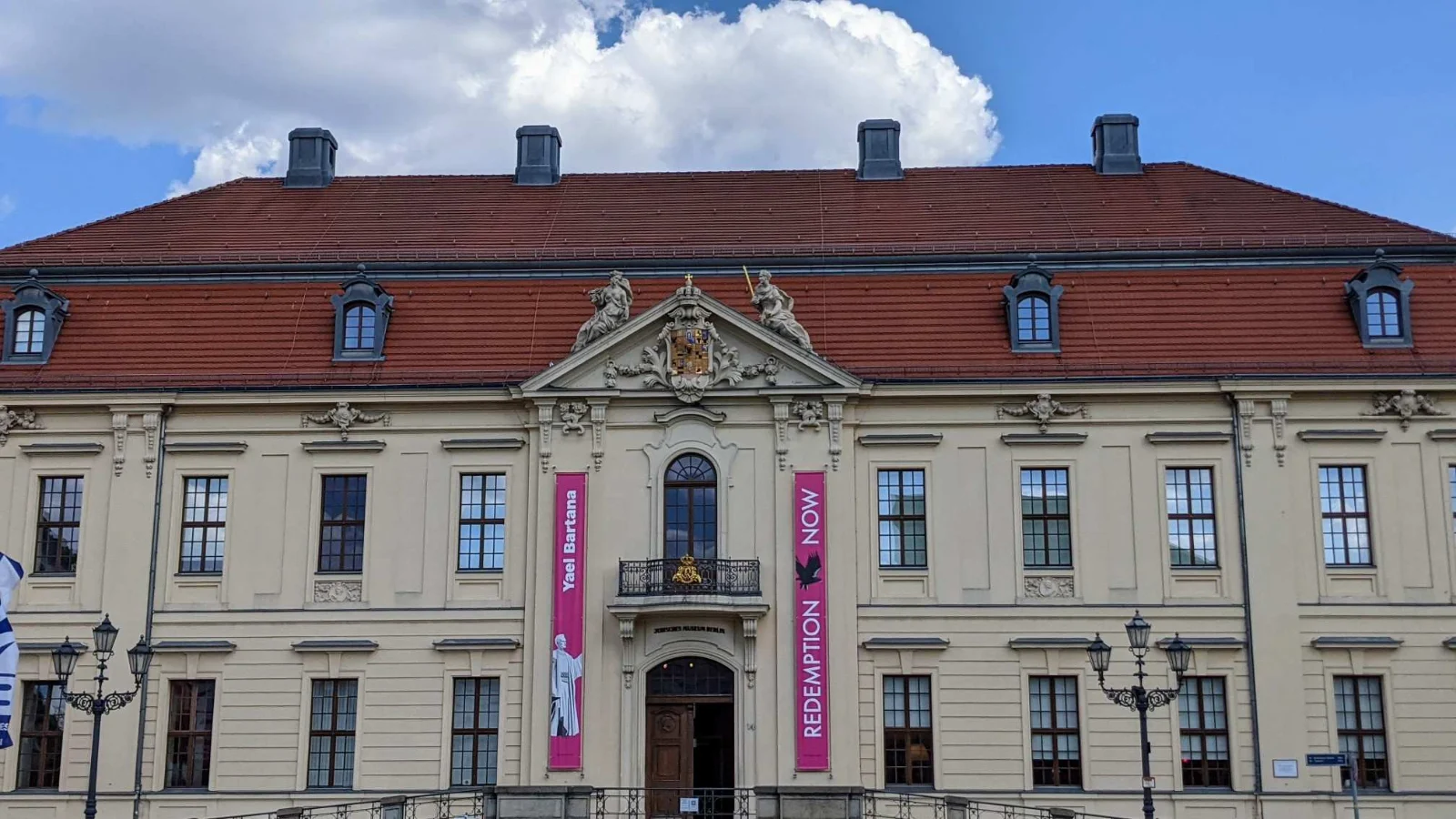 Barocker Altbau des Jüdischen Museums Berlin mit Giebel, Portal und zwei pinken Bannern der Ausstellung Yael Bartana, Redemption Now