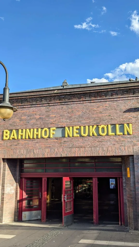 Backsteinfassade des Bahnhofs Neukölln mit gelben Einzelbuchstaben und roten Türen