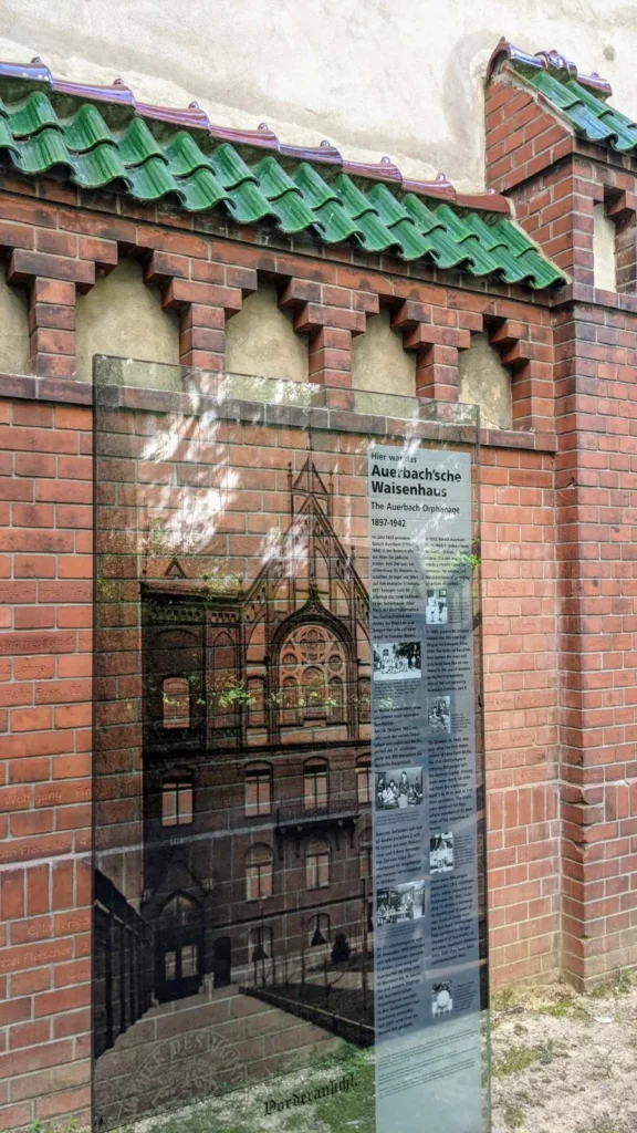 Glasstele Ich war hier mit historischer Ansicht des Waisenhauses vor der erhaltenen Klinkermauer mit den Namen der ermordeten Kinder