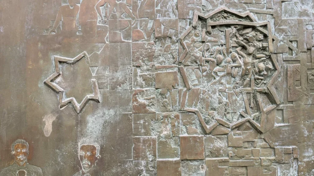 Bronzerelief der Flatow-Stele mit Turnern, zwei eingravierten Männerporträts und einem sternförmigen Rahmen, in dem ein Knäuel stürzender Figuren zu sehen ist