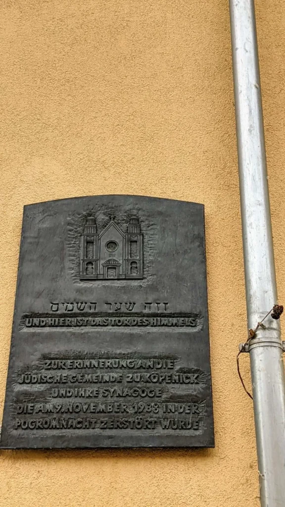 Bronzene Gedenktafel mit dem Relief einer Synagogenfassade und hebräischer Inschrift an einer ockergelben Putzwand in der Köpenicker Freiheit