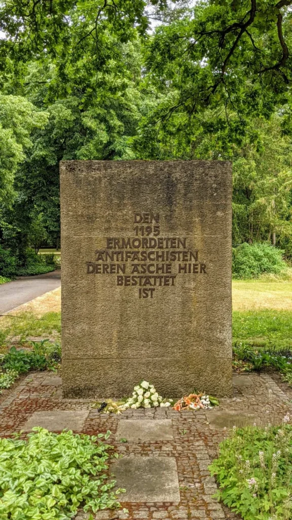 Gedenkstein mit Bronzebuchstaben für 1195 ermordete Antifaschisten im Ehrenhain des Friedhofs Baumschulenweg, am Fuß abgelegte Blumen