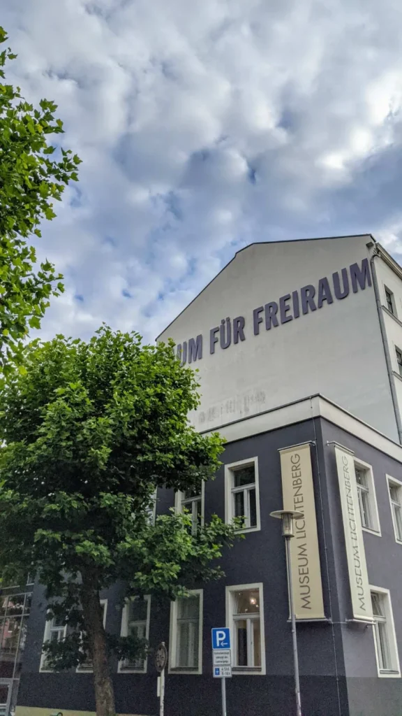 Eckgebäude mit Fahnenbannern Museum Lichtenberg und dem Giebelschriftzug Raum für Freiraum unter Schäfchenwolken