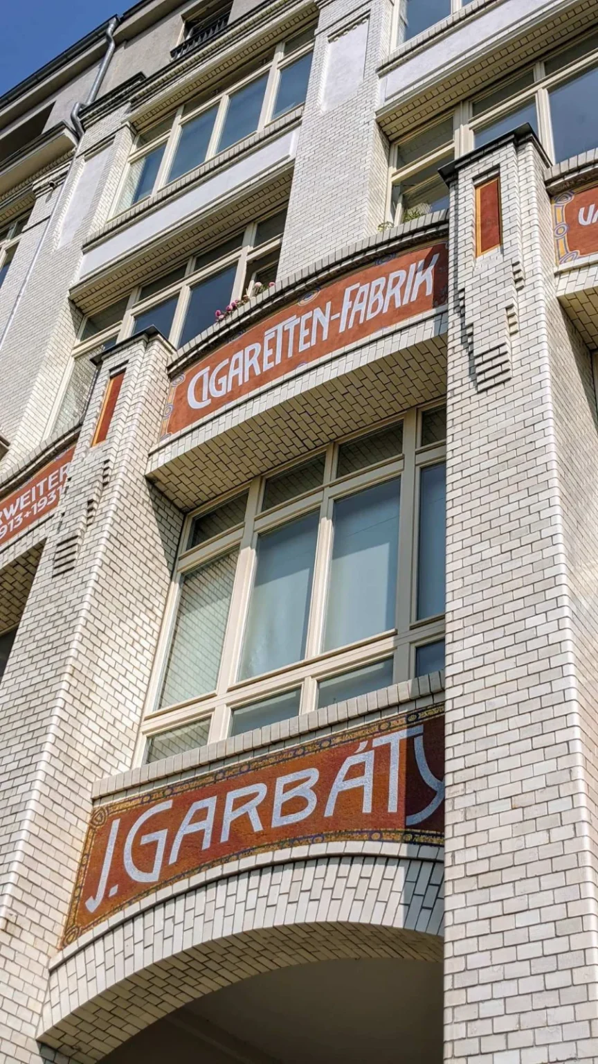 Fassade aus weiß glasierten Ziegeln mit Erkern und den Schriftfeldern Cigaretten-Fabrik J. Garbáty