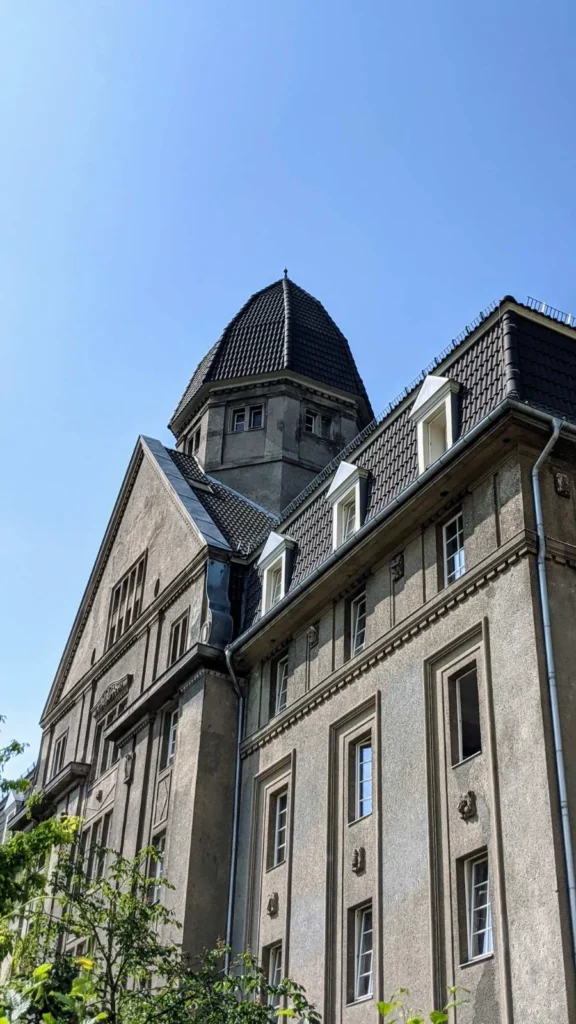 Grau verputztes Fabrikgebäude der Zigarettenfabrik Garbáty mit geschweifter Turmhaube, Giebel und Gauben unter blauem Himmel