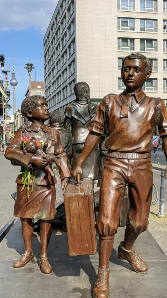 Bronzene Kinderfiguren am Bahnhof Friedrichstraße, vorn ein Mädchen mit Teddybär und ein Junge mit Koffer