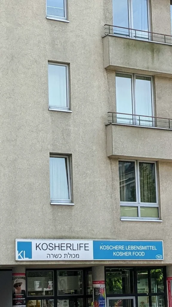 Laden Kosherlife mit blau-weißem Schild in einer grau verputzten Hausfassade in der Brunnenstraße